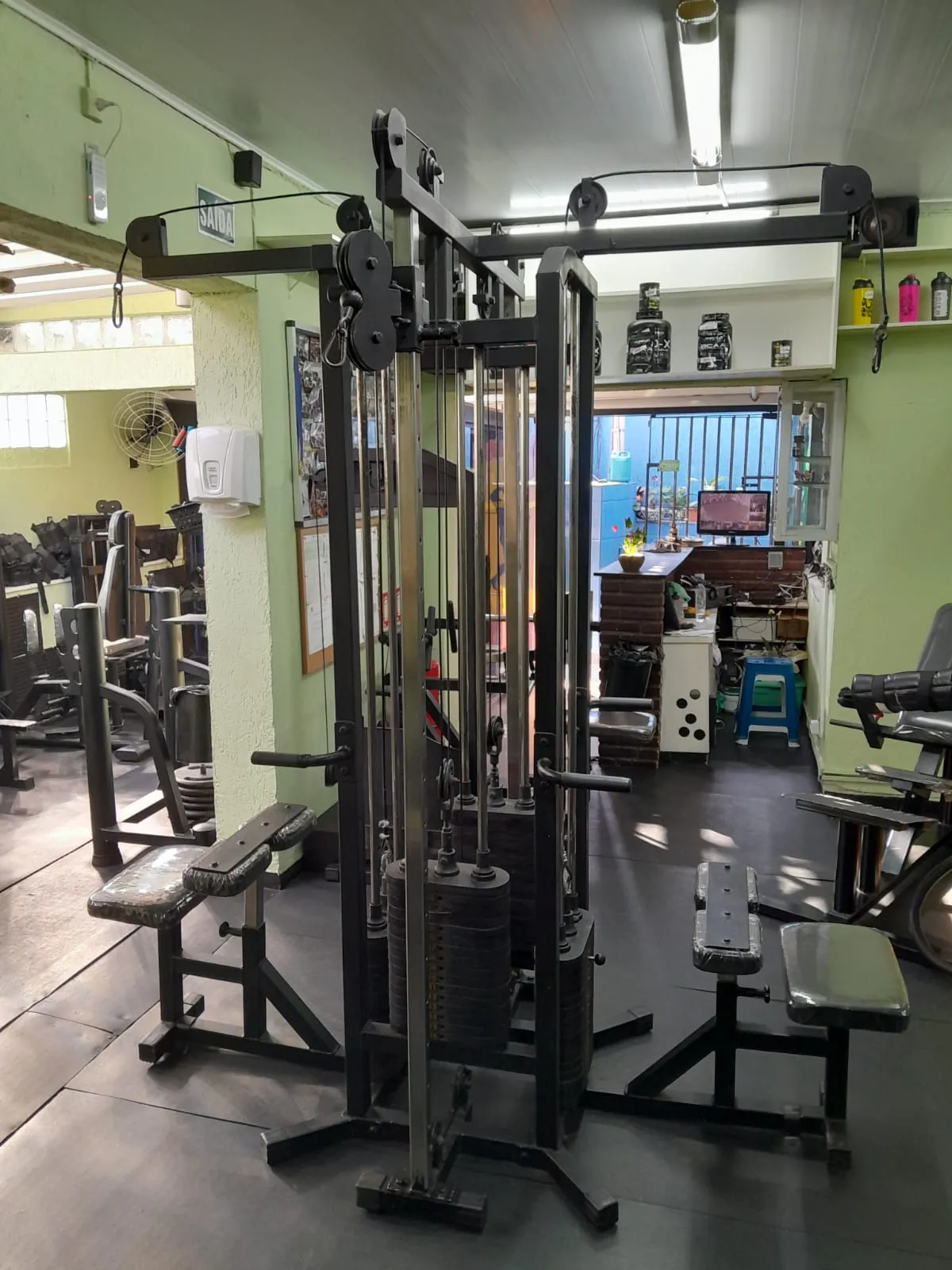Área de musculação com estação de cabos e, ao fundo, a recepção