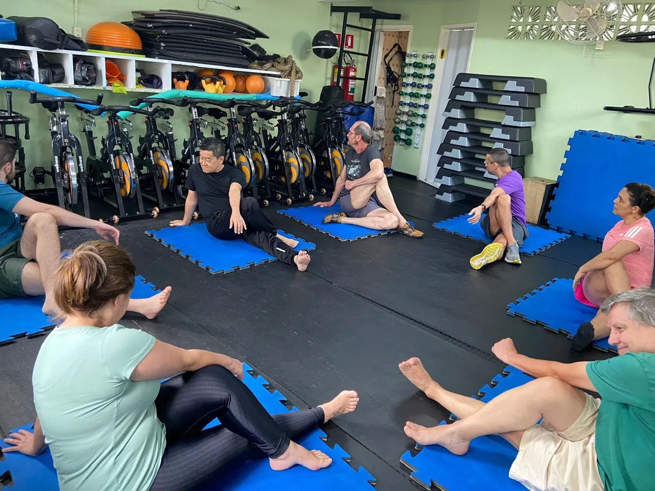 Turma de mat pilates sentada nos tatames azuis, fazendo torção de tronco